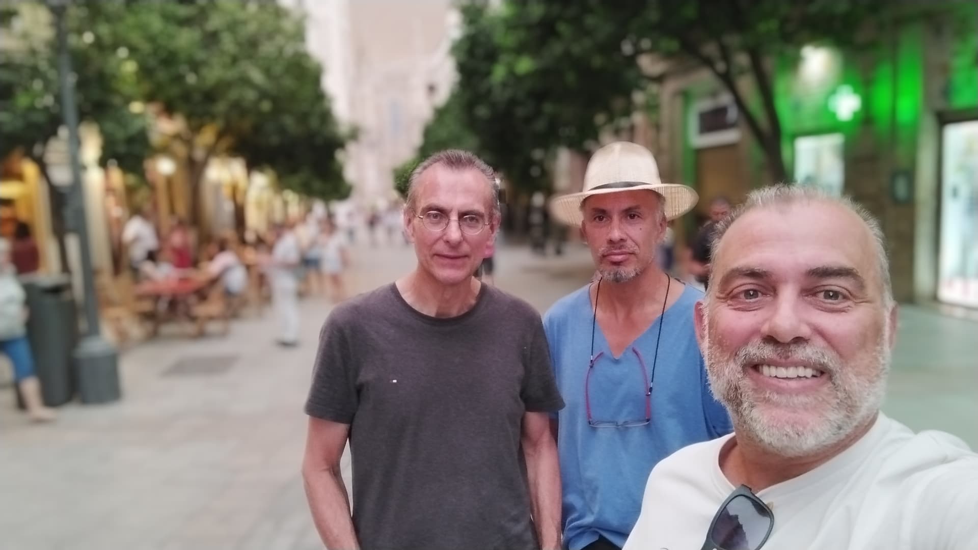 Johnny smiling with two travelers on a leafy pedestrian street in Seville